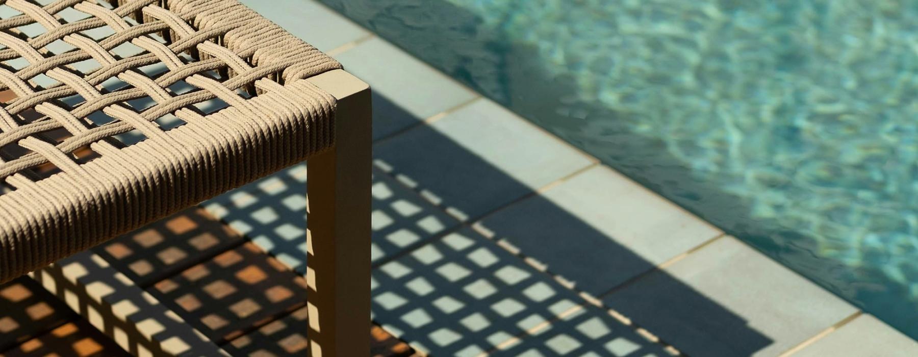 A lounge chair next to a pool in the sun.