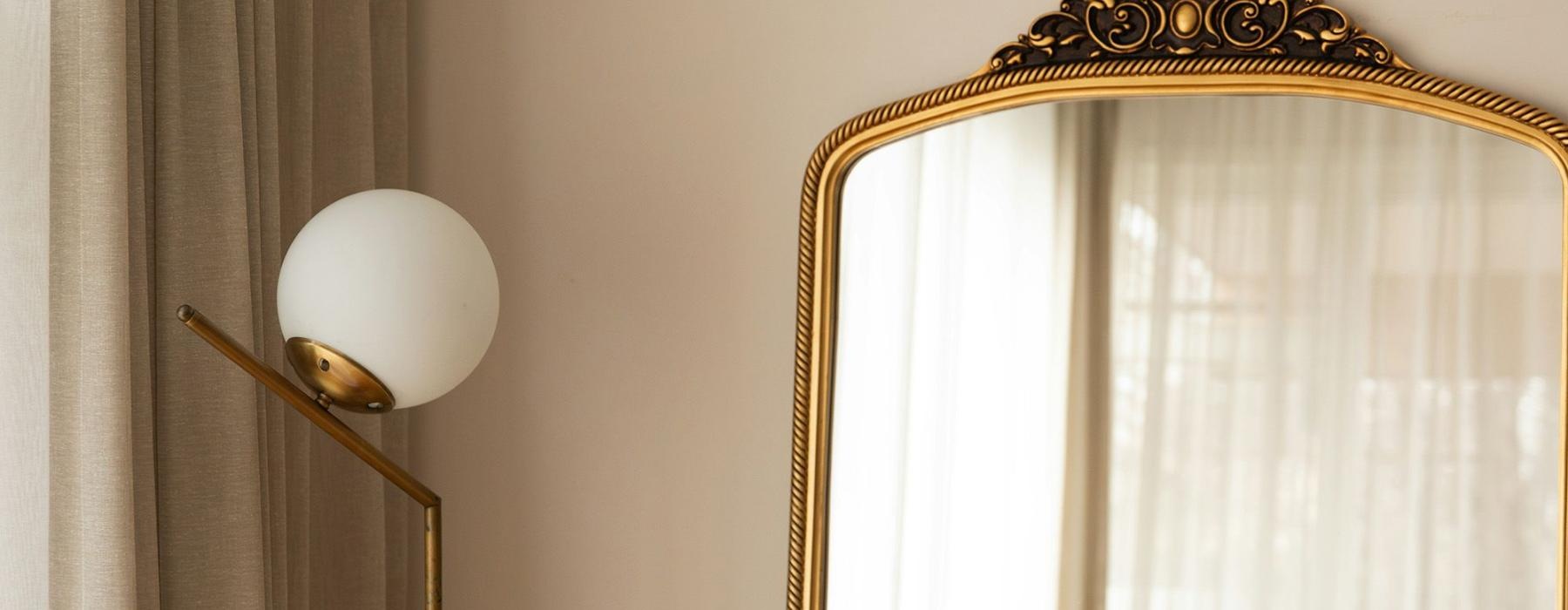 A large mirror next to a lamp and window.