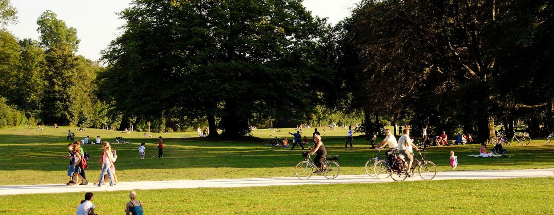 A park with many people riding bikes, having a picnic, and walking.